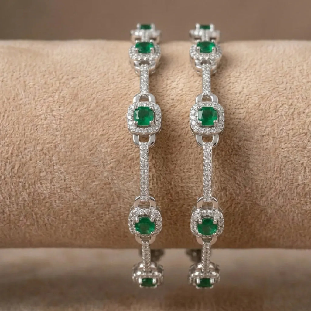 Elegant silver floral bangle featuring emerald green stones on a professional display.