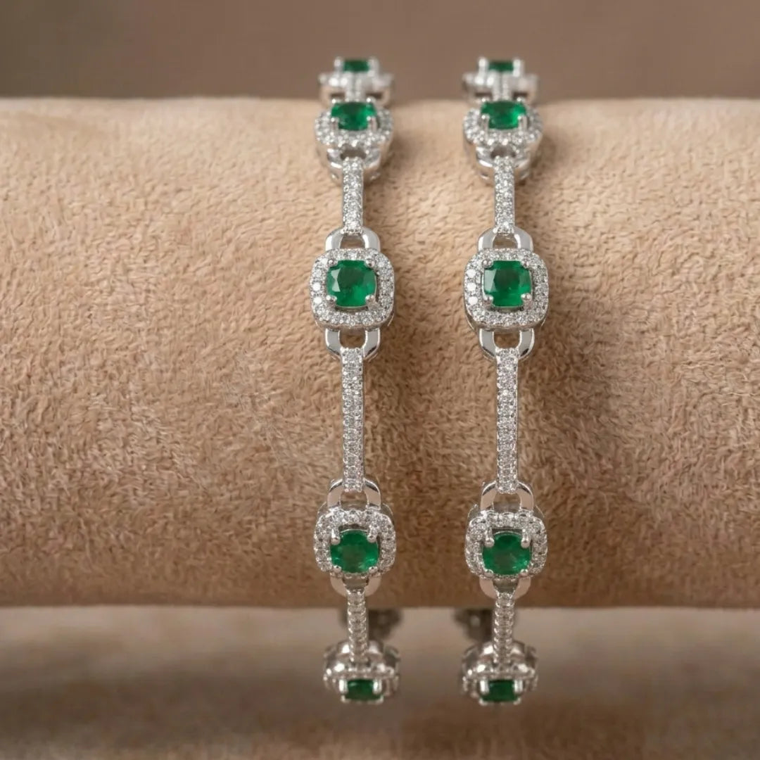 Elegant silver floral bangle featuring emerald green stones on a professional display.
