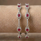 Silver-plated eternity bangle with red gemstones and white zirconia floral design.