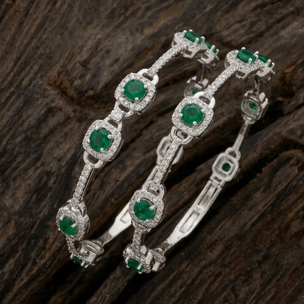 Elegant silver floral bangle featuring emerald green stones on a professional display.