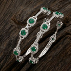 Elegant silver floral bangle featuring emerald green stones on a professional display.