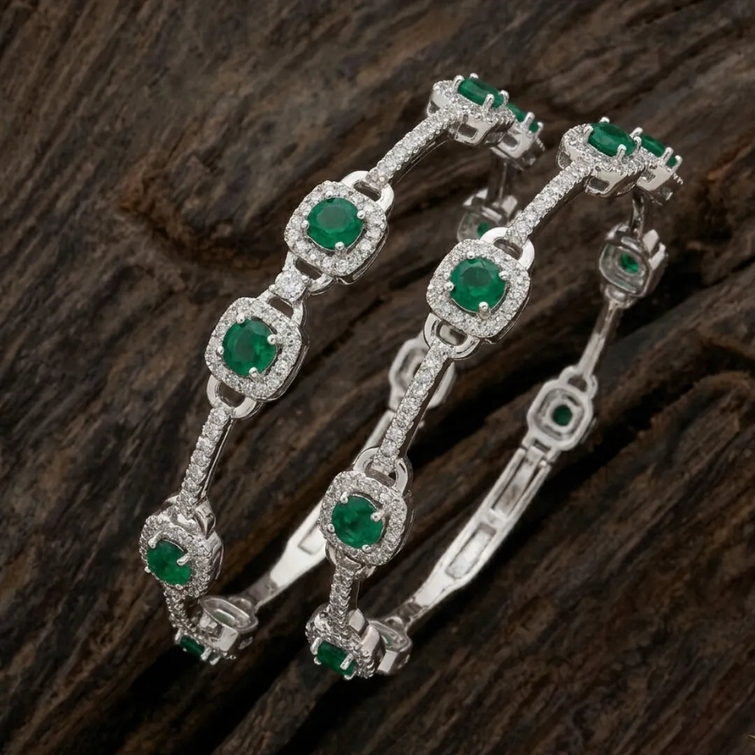 Elegant silver floral bangle featuring emerald green stones on a professional display.