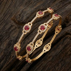 Gold-plated eternity bangle with red center stones and white floral zirconia design.