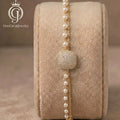Golden cushion-cut zirconia layered bracelet featuring white pearls on a professional display stand.