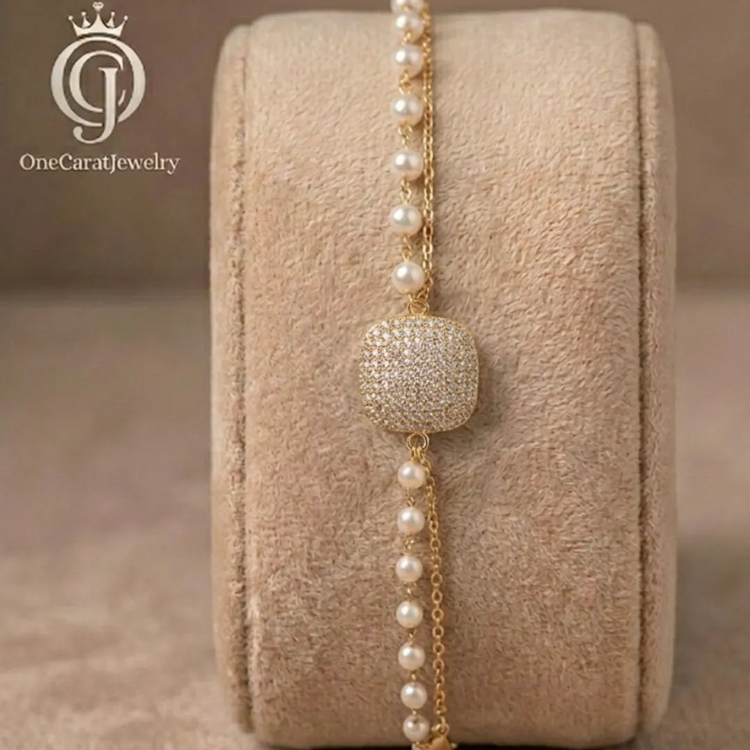 Golden cushion-cut zirconia layered bracelet featuring white pearls on a professional display stand.