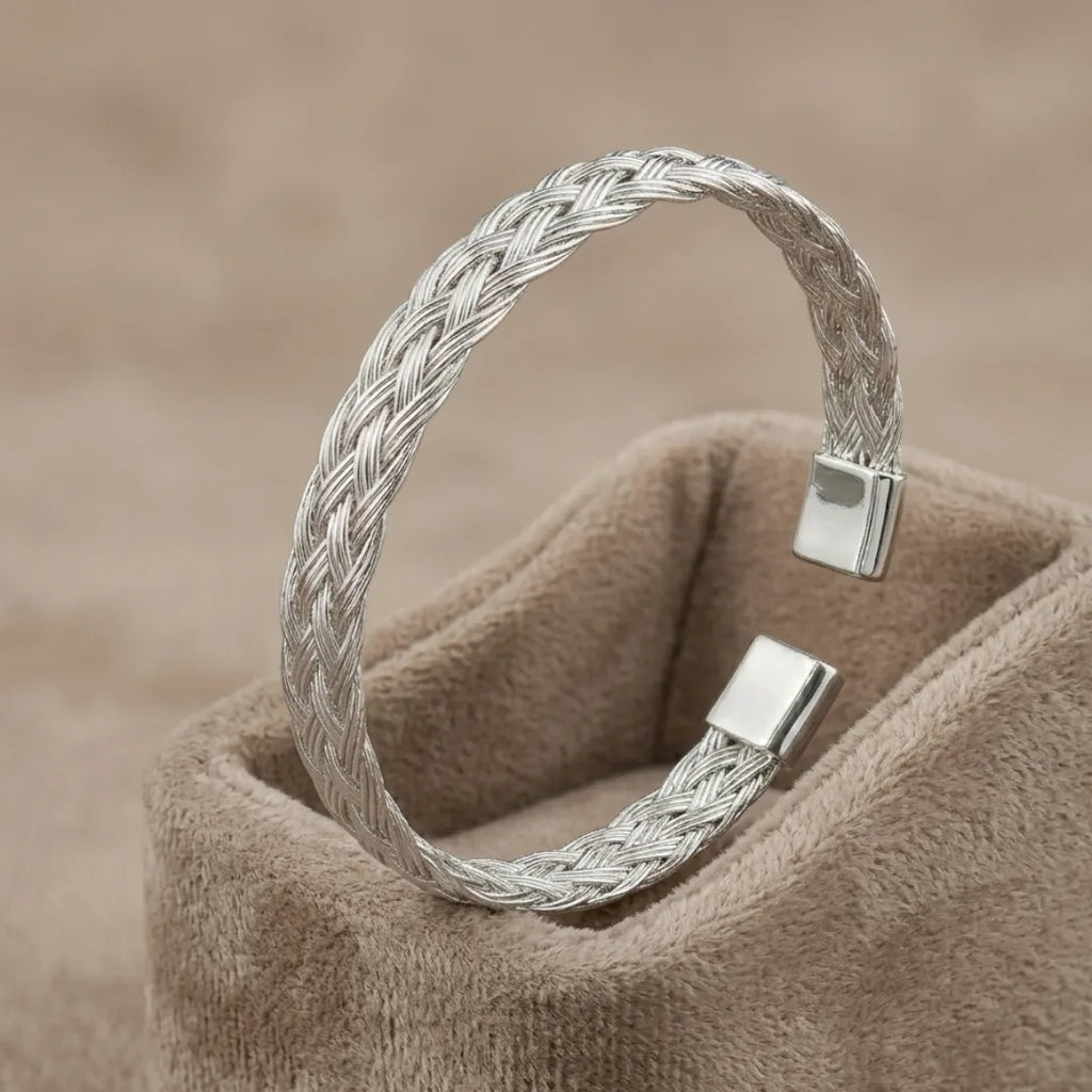 High-polish twisted stainless steel cuff bracelet on a minimalist display stand.