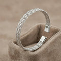 High-polish twisted stainless steel cuff bracelet on a minimalist display stand.