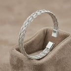 High-polish twisted stainless steel cuff bracelet on a minimalist display stand.