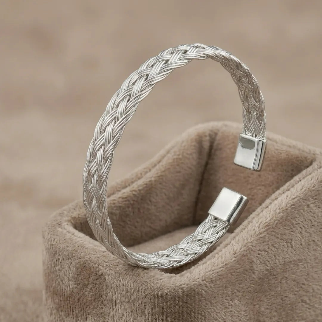 High-polish twisted stainless steel cuff bracelet on a minimalist display stand.