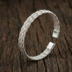 High-polish twisted stainless steel cuff bracelet on a minimalist display stand.