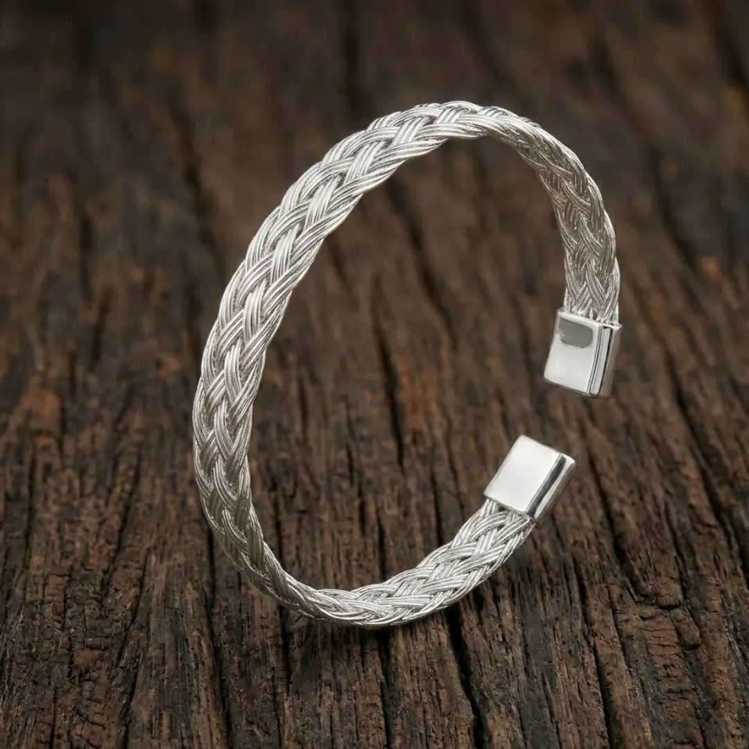 High-polish twisted stainless steel cuff bracelet on a minimalist display stand.
