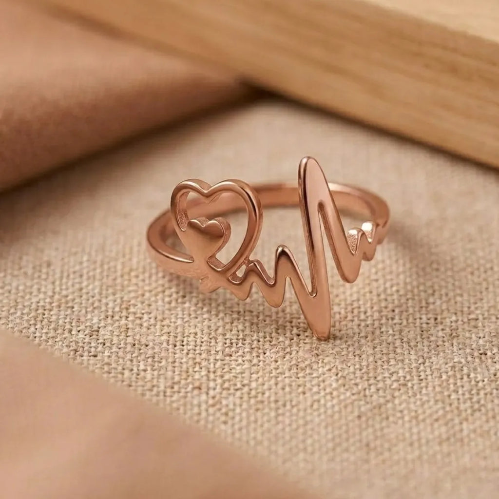Rose gold ring with heart and heartbeat design on a beige fabric background