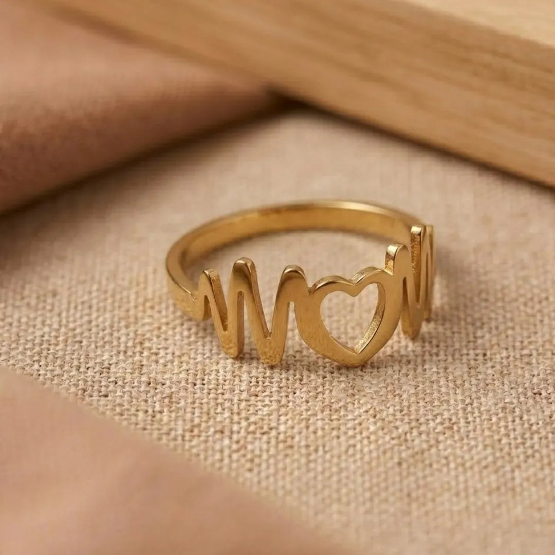 Gold ring with 'mom' and heart design on a beige fabric background