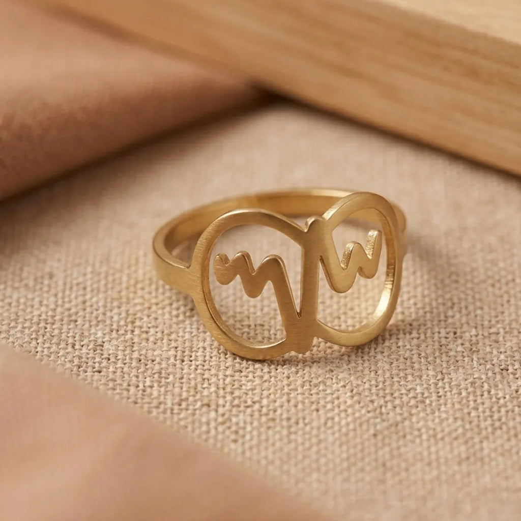 Gold ring with cut-out letter design on a beige fabric background
