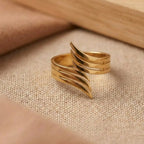 Gold ring with wavy design on a beige fabric background