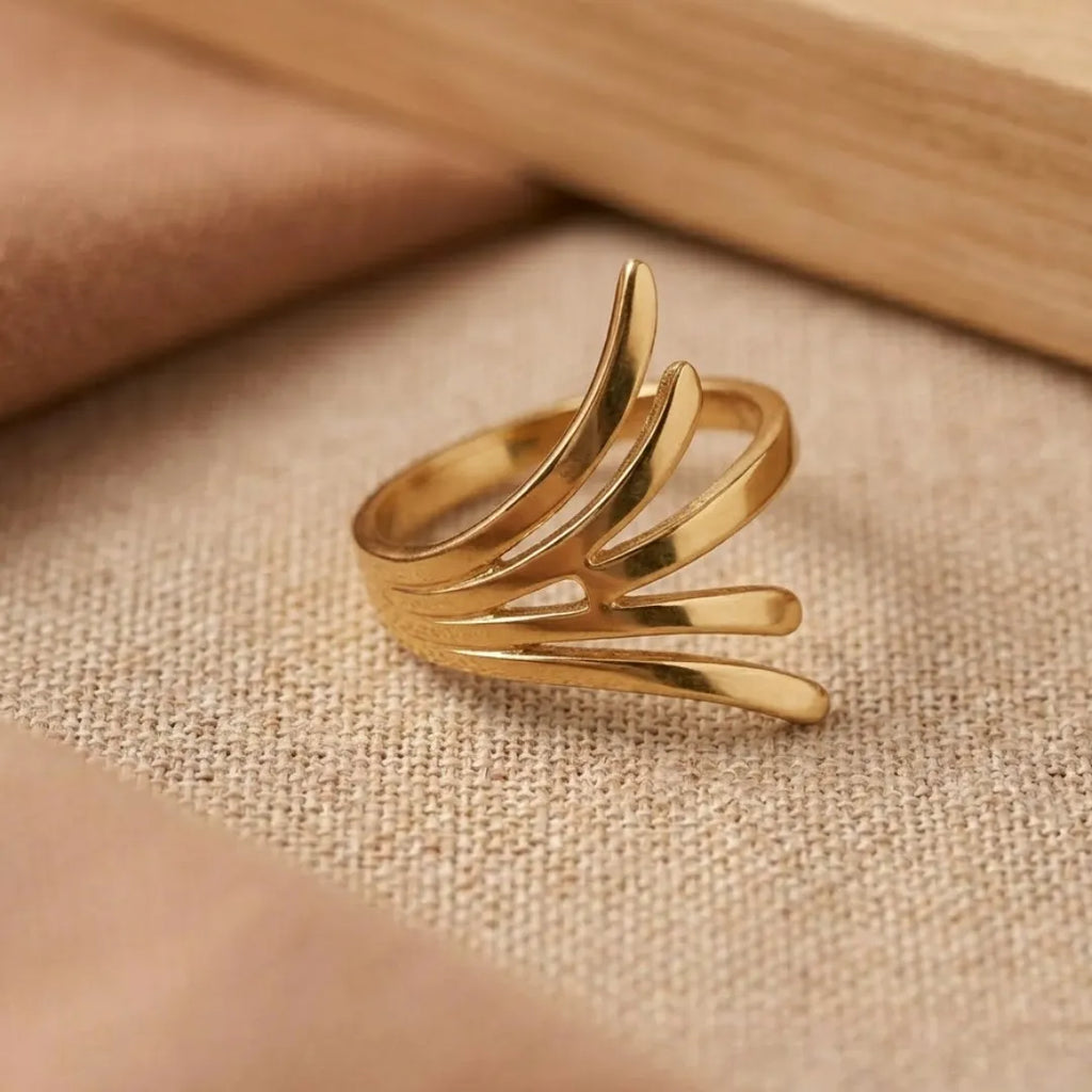 Gold ring with a leaf-like design on a beige fabric background