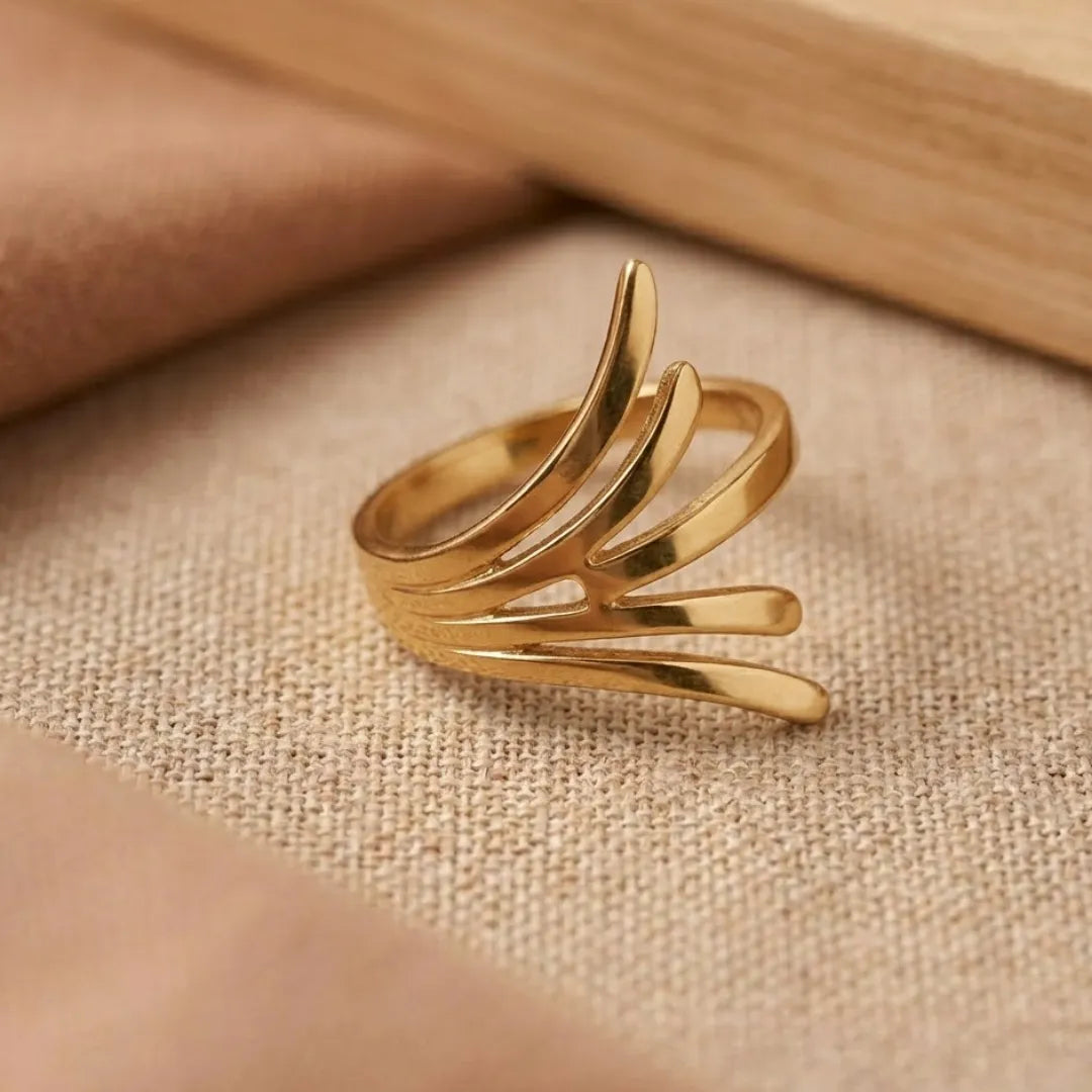 Gold ring with a leaf-like design on a beige fabric background