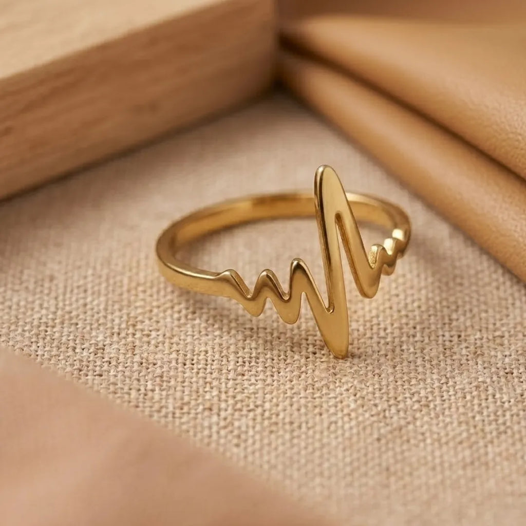 Gold ring with a heart rate design on a beige fabric background