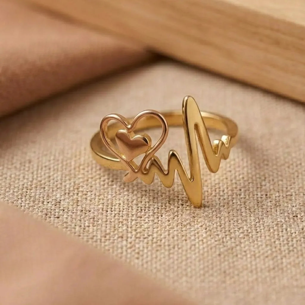 Gold ring with heart and heartbeat line design on a beige fabric background