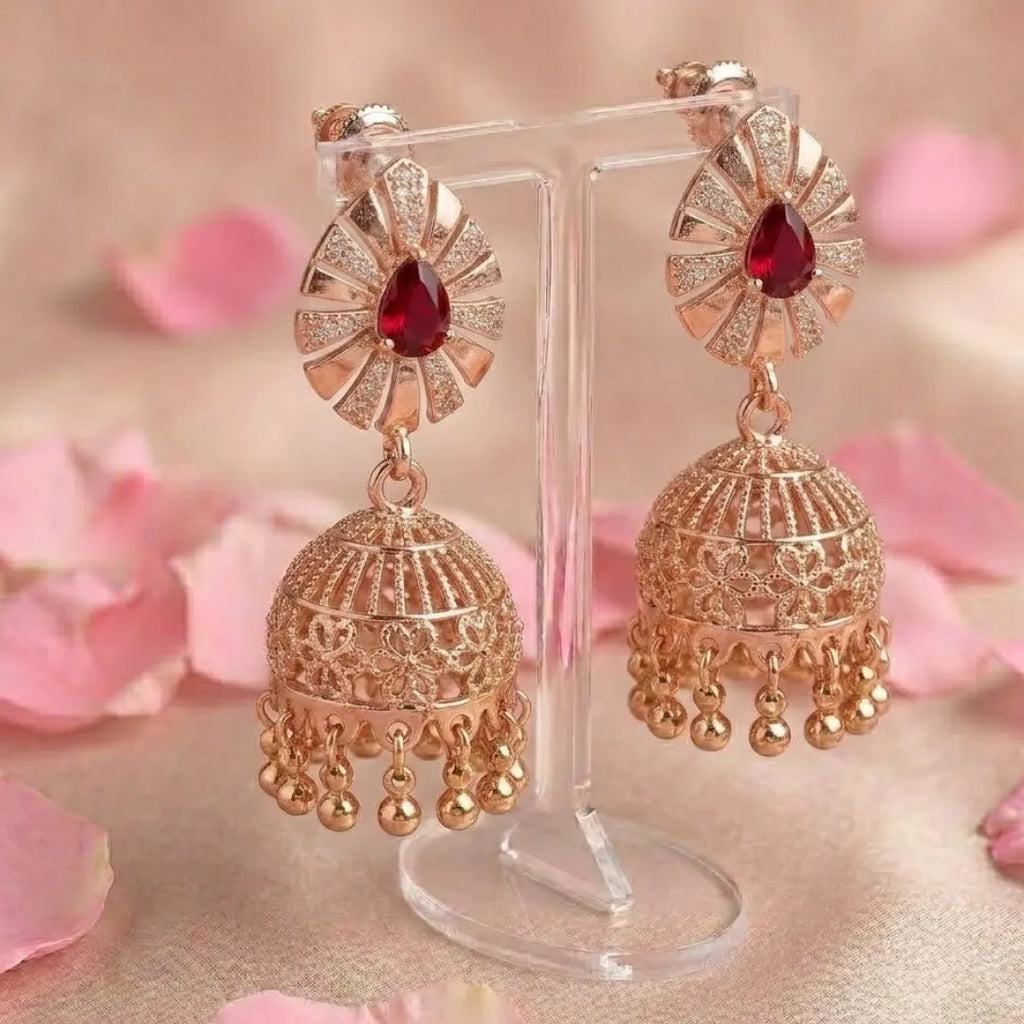 Gold earrings with red gemstones on a stand with pink floral background