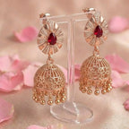 Gold earrings with red gemstones on a stand with pink floral background