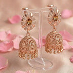 Rose gold earrings on a stand with pink petals in the background