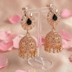 Rose gold earrings with black gemstones on a stand with pink floral background