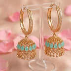 Gold hoop earrings with turquoise drops on a stand with pink floral background