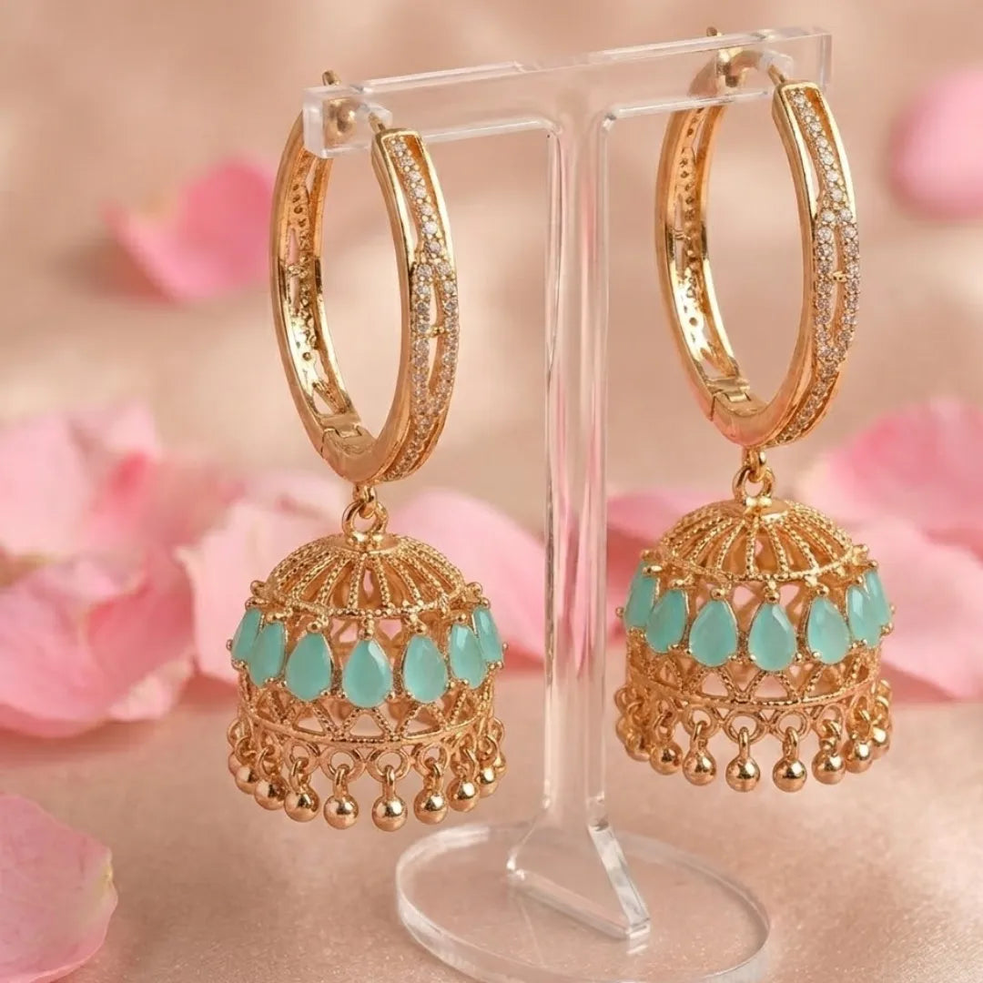 Gold hoop earrings with turquoise drops on a stand with pink floral background