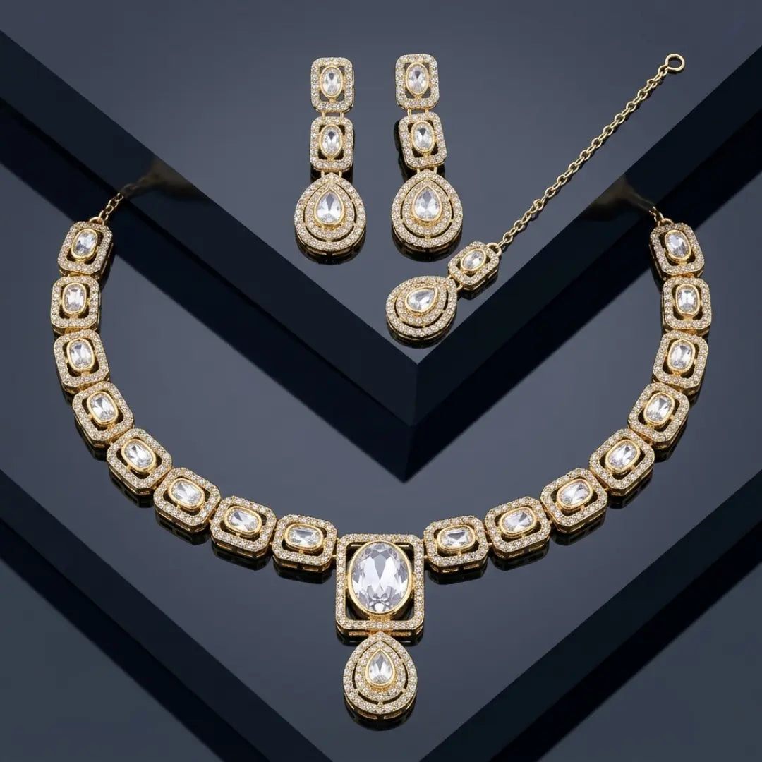 Royal gold-plated necklace set with large crystals and maang tikka on a black reflective surface.