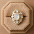 Gold ring with a large central stone and smaller stones on a beige cushion