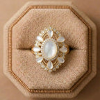 Gold ring with a large central stone and smaller stones on a beige cushion
