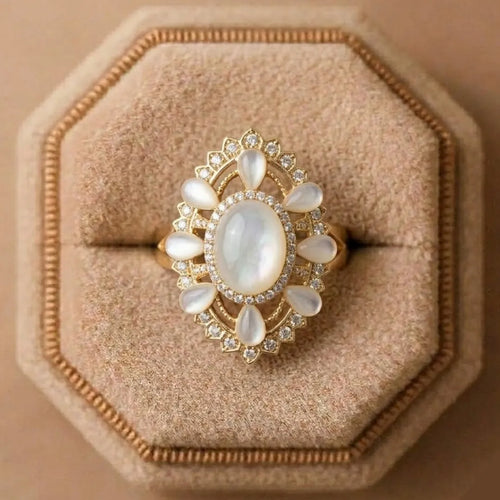 Gold ring with a large central stone and smaller stones on a beige cushion