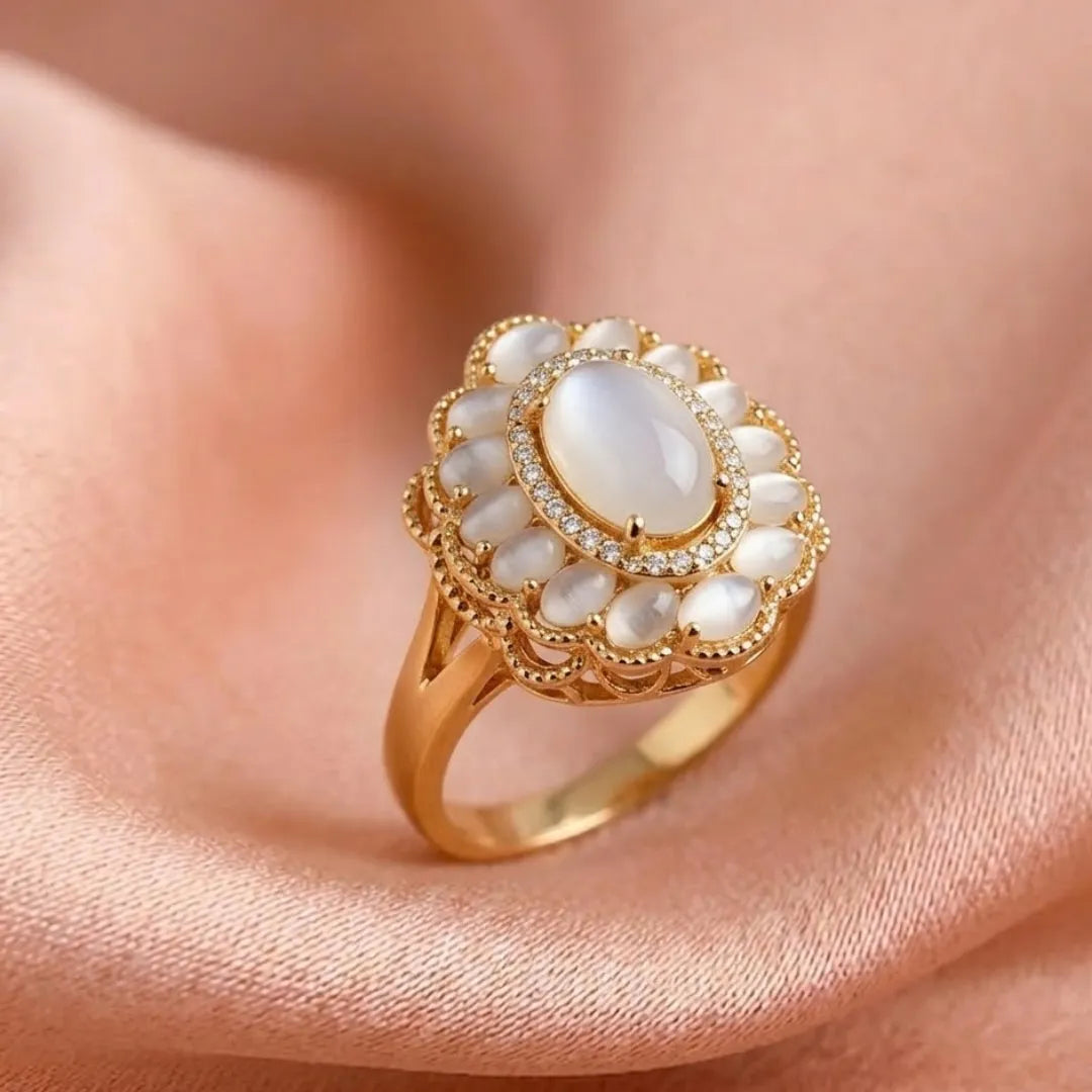 Gold ring with a large central gemstone and smaller stones on a soft pink fabric background