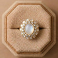 Gold ring with a large central gemstone and smaller stones on a beige cushion