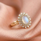 Gold ring with a central gemstone and pearl-like stones on a soft pink fabric background
