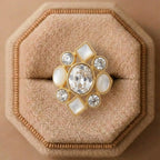 Gold ring with large central gemstone and smaller stones on a beige cushion