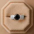 Ring with a black gemstone and diamond accents on a beige cushion