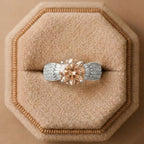 Diamond ring with a pinkish-brown center stone on a beige cushion in a jewelry box.