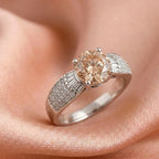 Diamond ring with a peach-colored center stone on a soft pink background