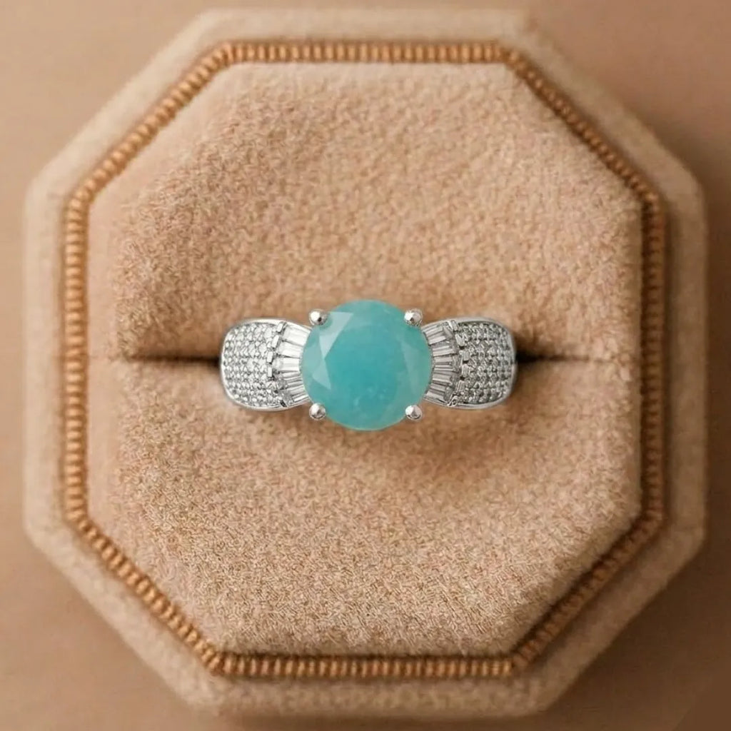 Turquoise gemstone ring with silver prongs on a beige cushion