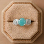 Turquoise gemstone ring with silver prongs on a beige cushion